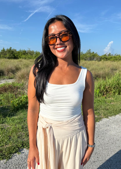 Woman wearing a white tank top and cream pants on a grass background