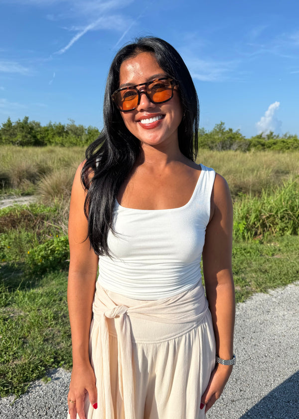 Woman wearing a white tank top and cream pants on a grass background