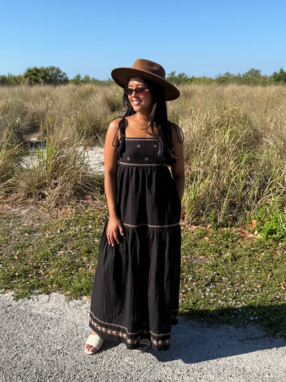 Woman in a black dress and hat standing in a natural setting