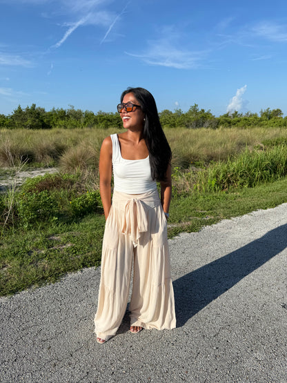 Woman wearing a white tank and shell colored pants on a grass background