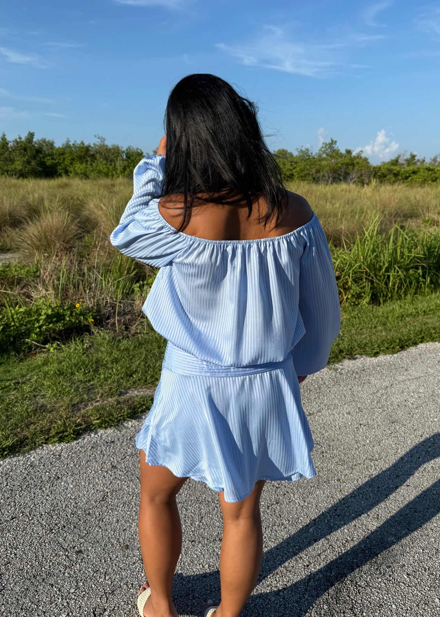 Girl wearing a blue off the shoulder long sleeve romper on a grass background