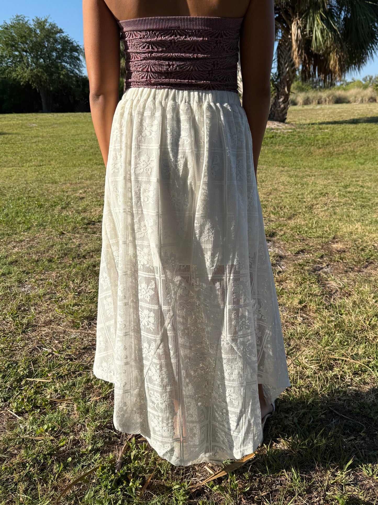 Person wearing a strapless top and long white skirt standing in a grassy field.