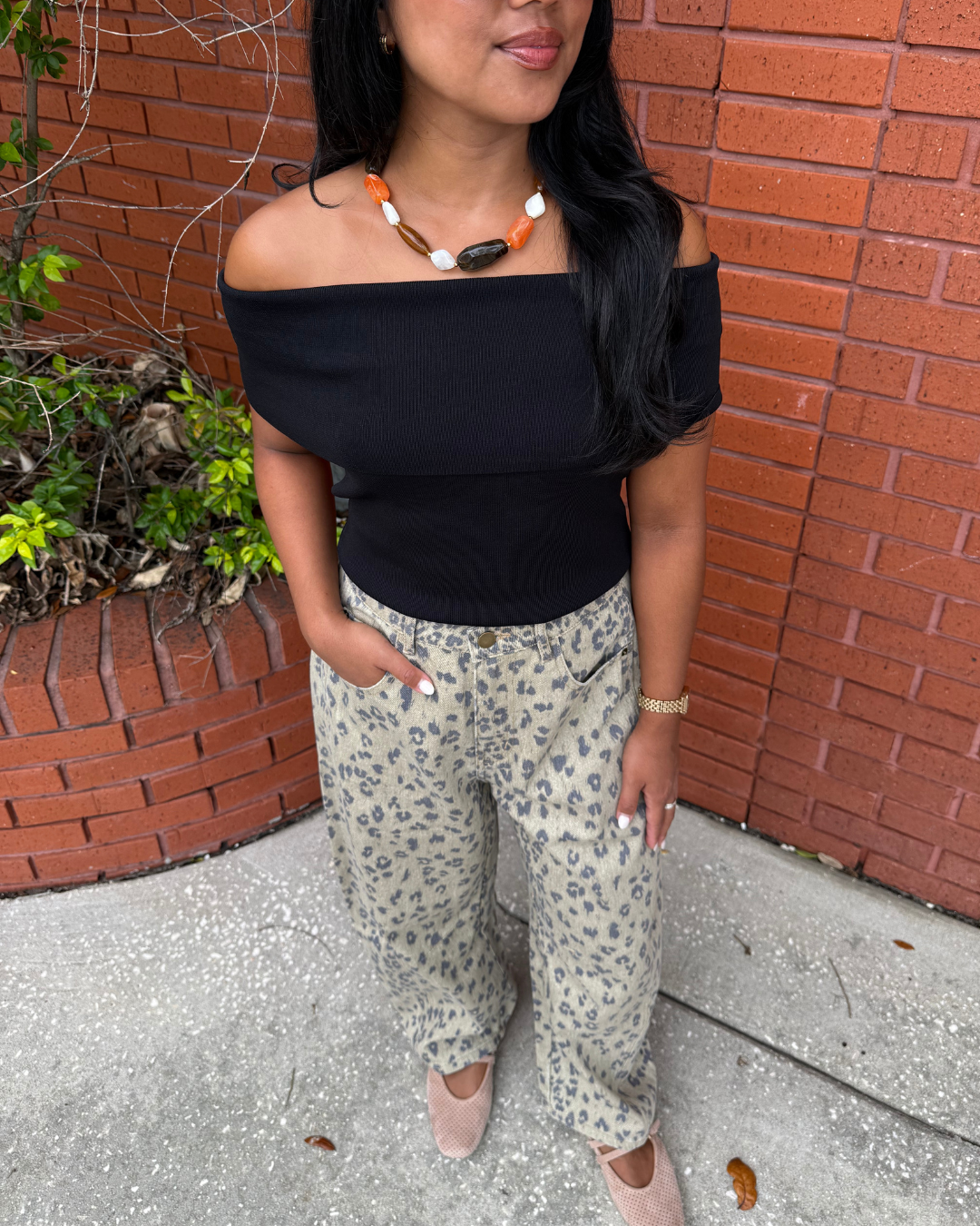 Women wearing a beaded orange, brown and white necklace with a black off the shoulder top and leopard pants