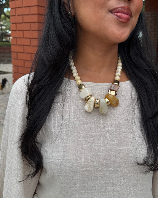 Girl wearing a beige top with a cream, gold, brown necklace
