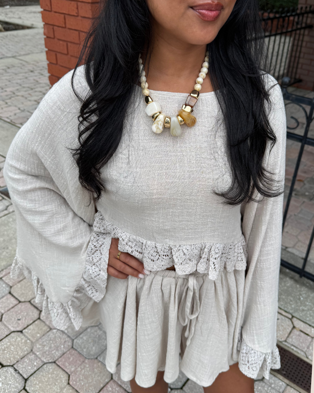 Girl wearing a beige top and shorts with a cream, gold, brown necklace