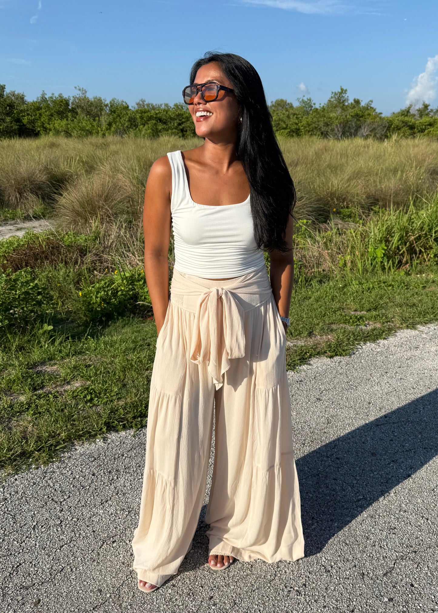 Woman wearing a white tank and shell colored pants on a grass background