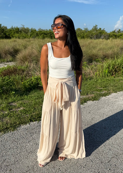 Woman wearing a white tank and shell colored pants on a grass background