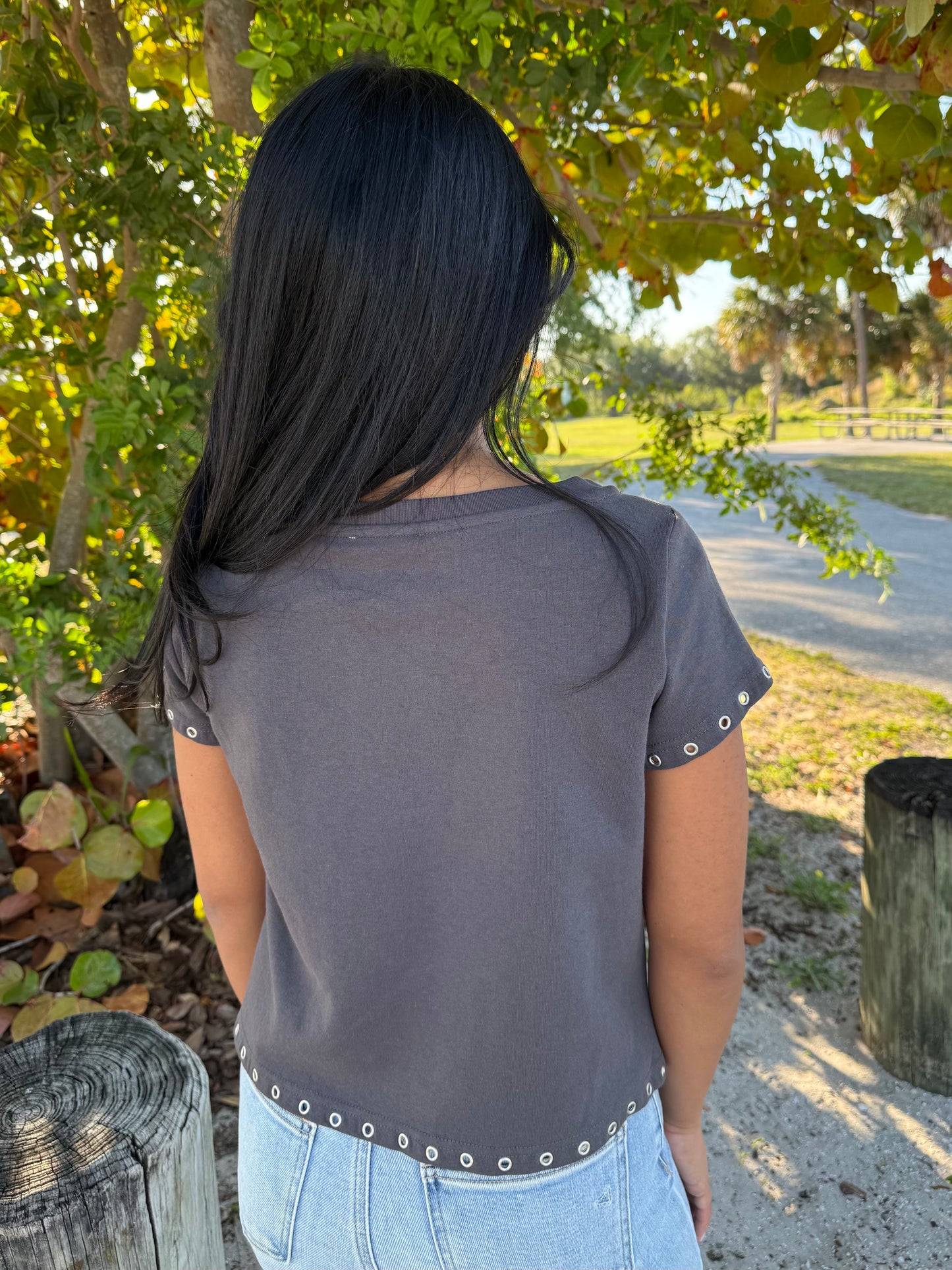 Person wearing a gray t-shirt with decorative trim in an outdoor setting