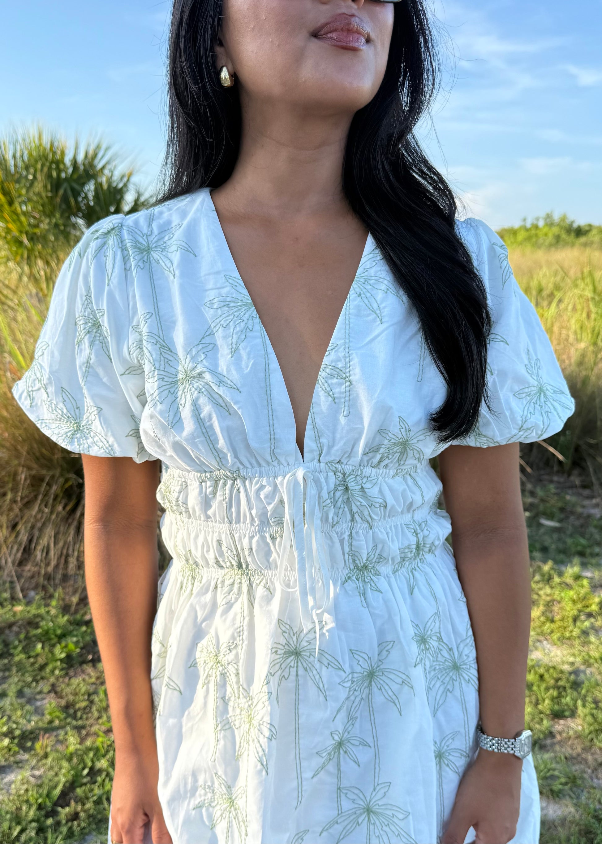 Girl wearing white mini dress with green palm tree print on a grass background.