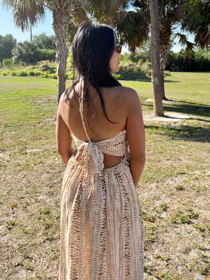 Woman in a long, open-back dress standing in a grassy area with trees.