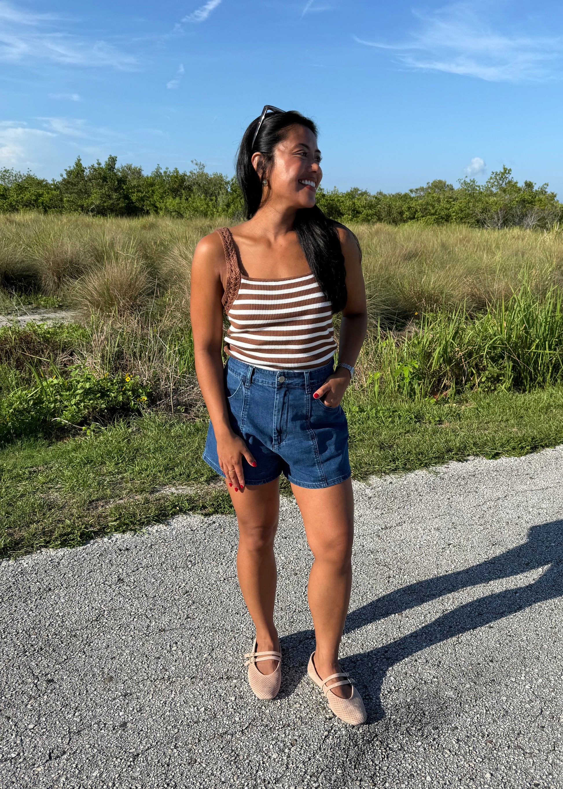 woman wearing a brown and white striped tank and jean shorts on a grass background