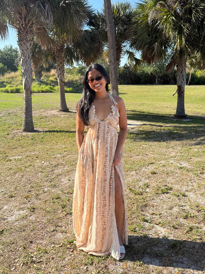 Woman in a long, patterned dress standing in a grassy area with palm trees.