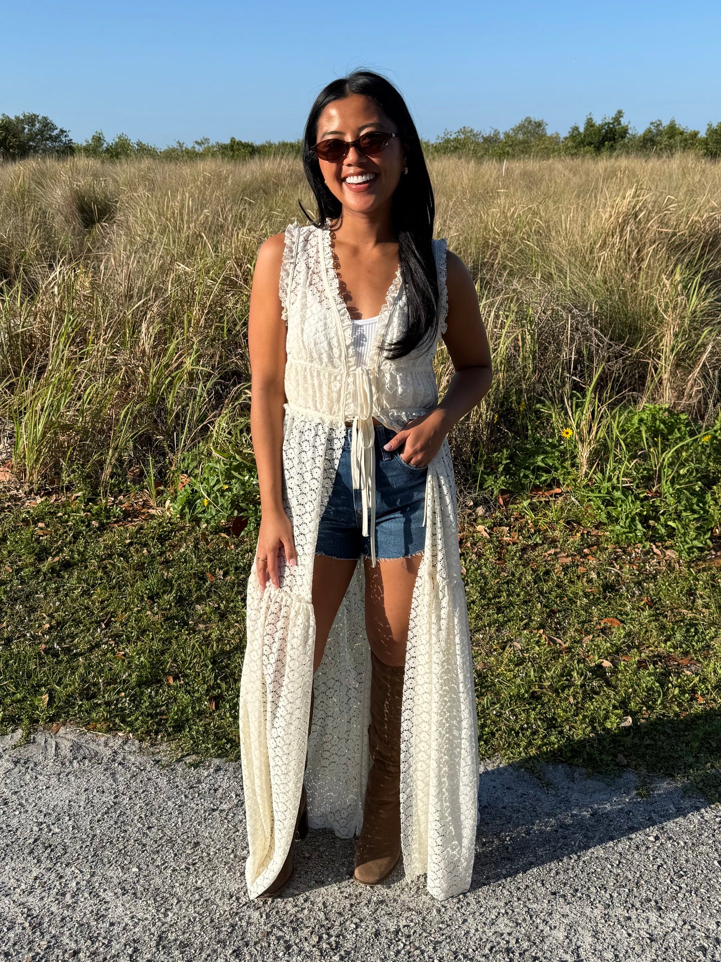 Woman wearing a long white lace dress standing in a natural setting with greenery.