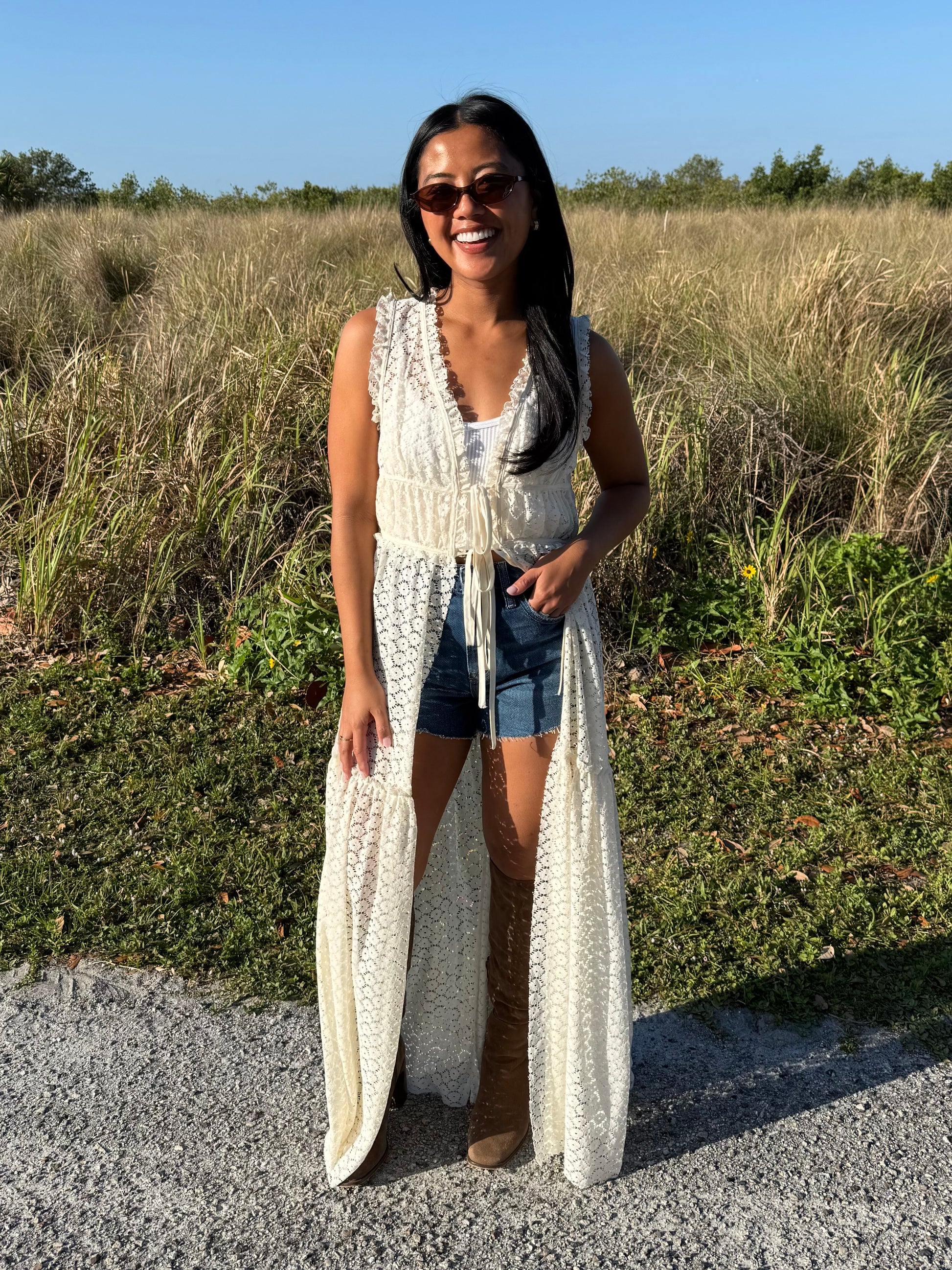 Woman wearing a long white lace dress standing in a natural setting with greenery.