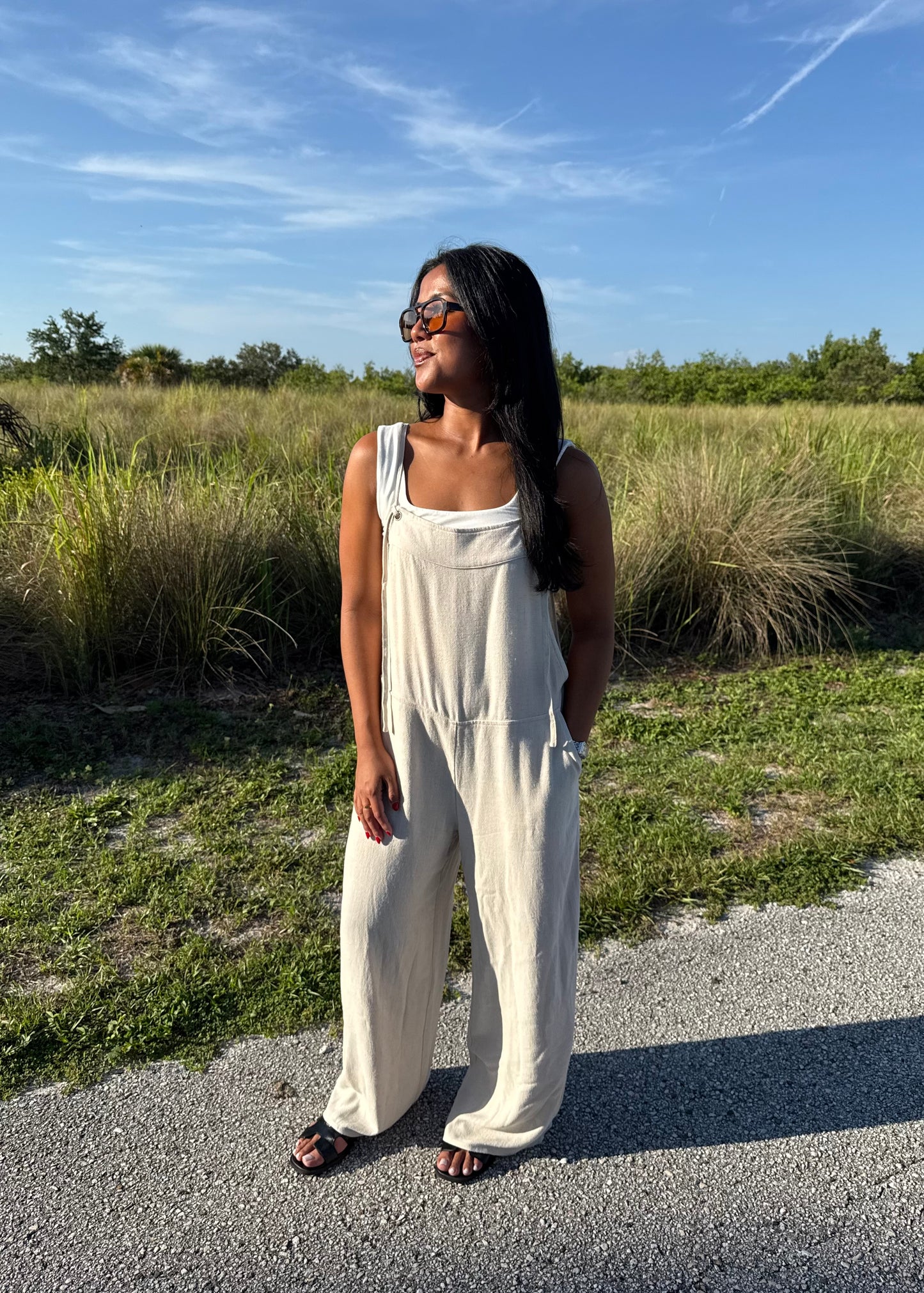 woman wearing a natural colored linen jumpsuit on a grass background