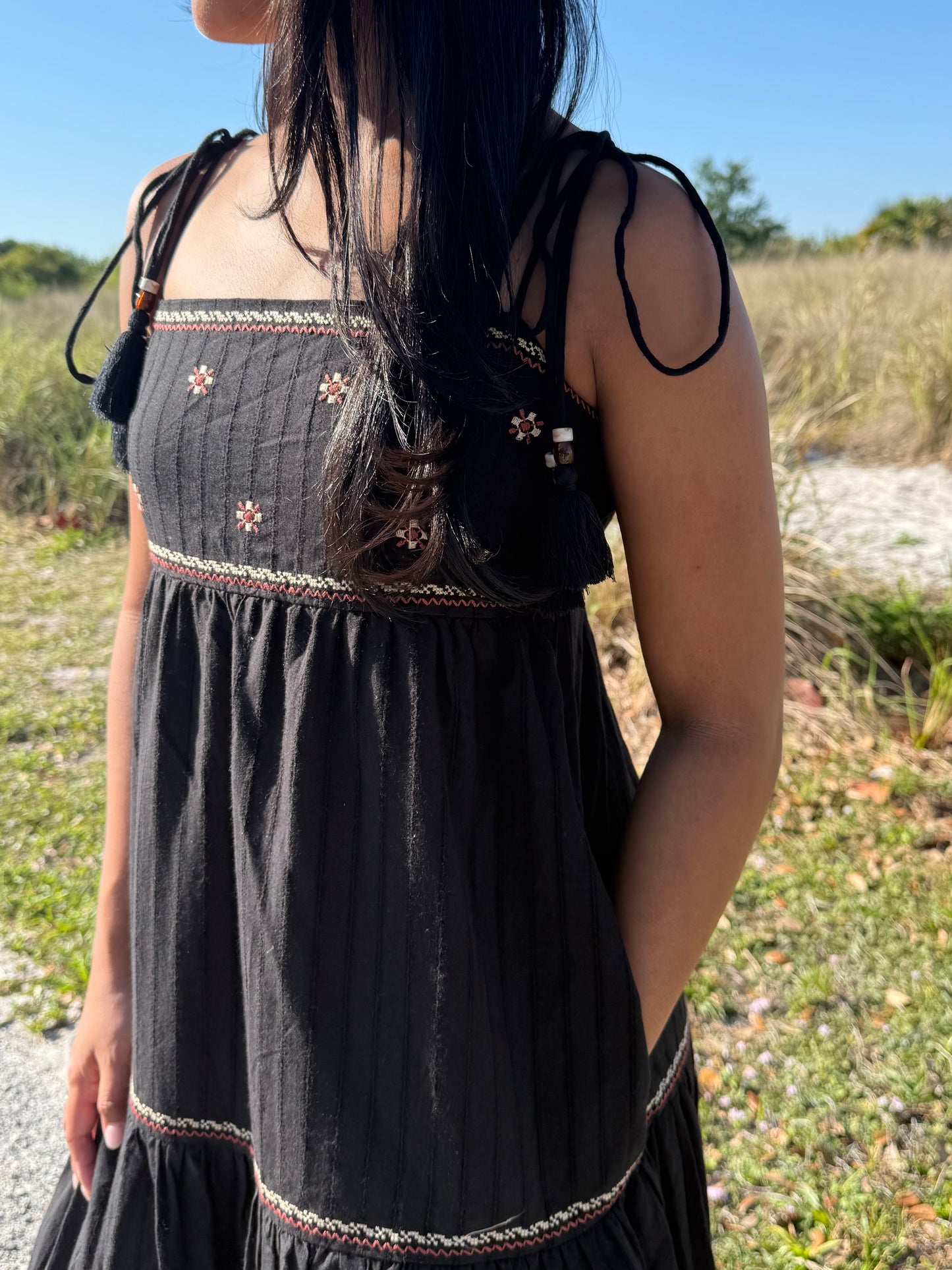 Person wearing a black dress with floral embroidery in an outdoor setting