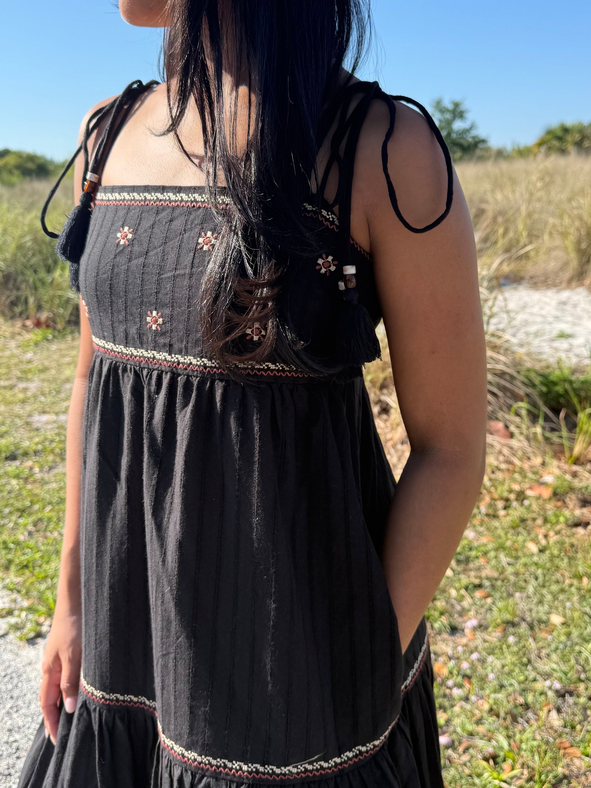 Person wearing a black dress with floral embroidery in an outdoor setting