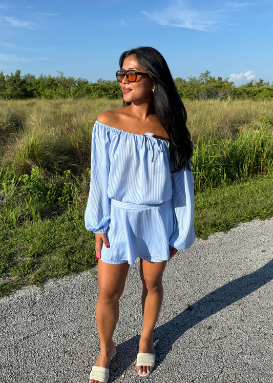 Girl wearing a blue off the shoulder long sleeve romper on a grass background