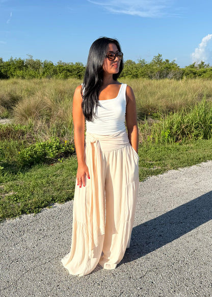 Woman wearing a white tank and shell colored pants on a grass background