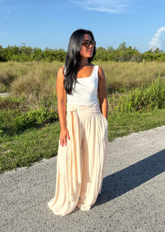 Woman wearing a white tank and shell colored pants on a grass background