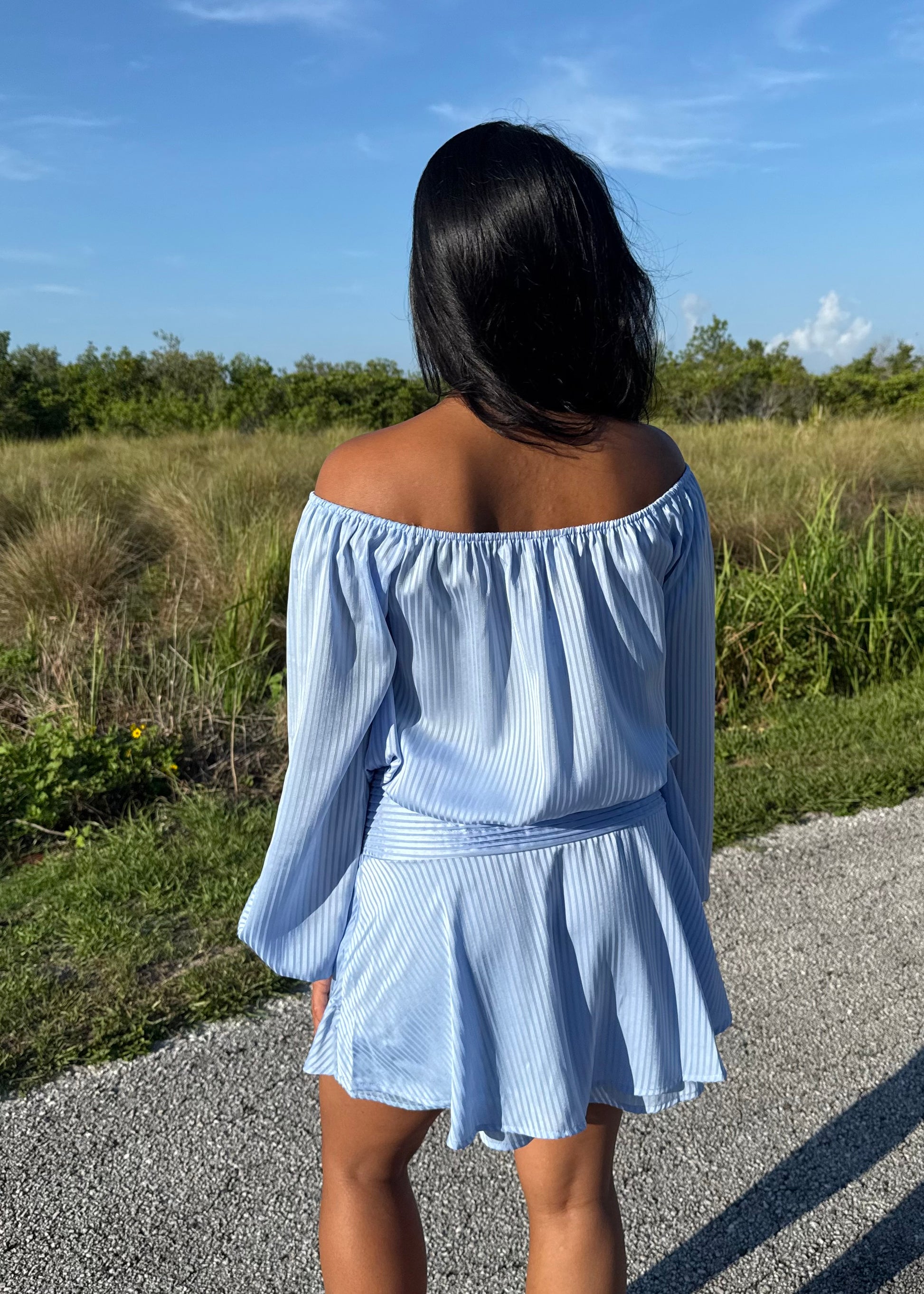 Girl wearing a blue off the shoulder long sleeve romper on a grass background