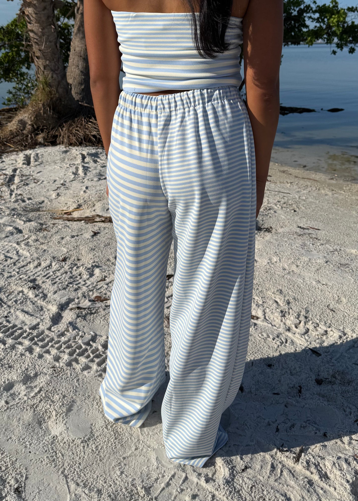 woman wearing striped top and striped pants on sand and water background
