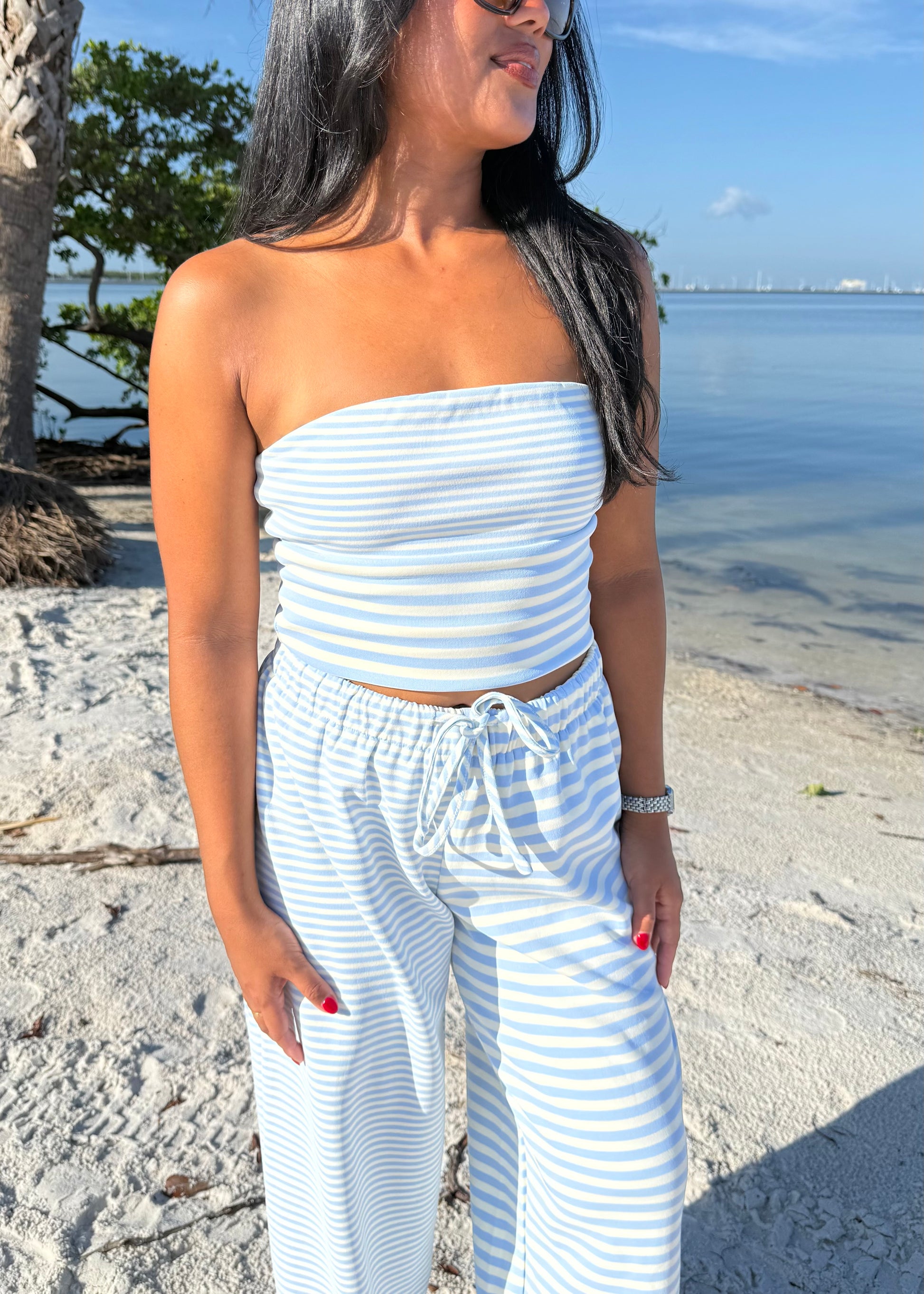 woman wearing striped top and striped pants on sand and water background