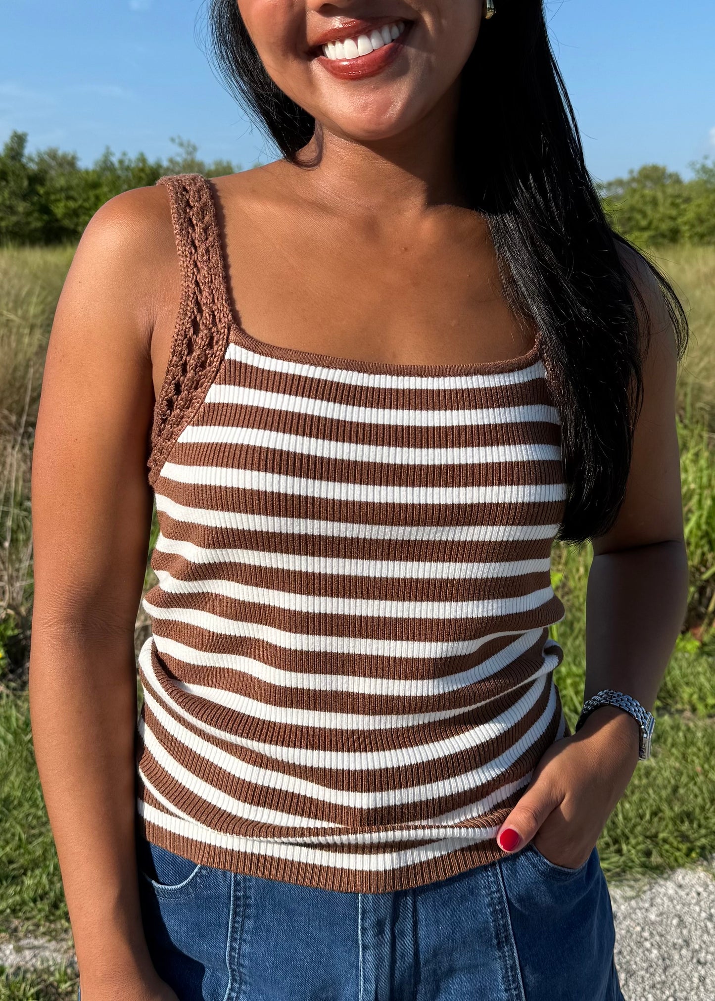 woman wearing a brown and white striped tank and jean shorts on a grass background