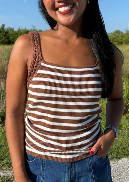 woman wearing a brown and white striped tank and jean shorts on a grass background