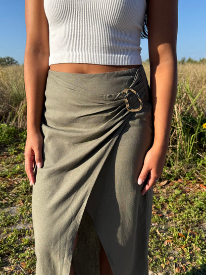 Person wearing a white top and olive green skirt in a natural setting