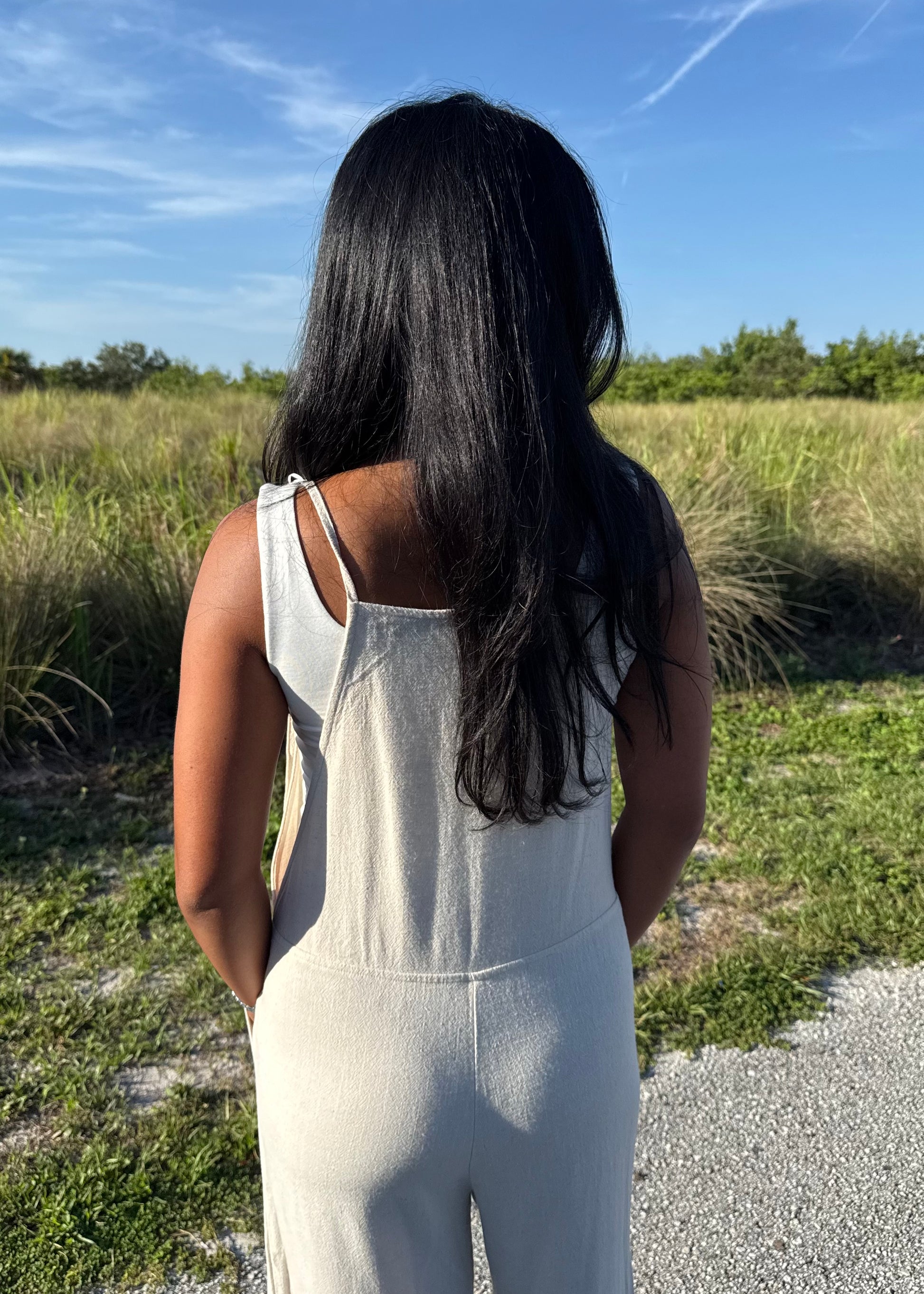 woman wearing a natural colored linen jumpsuit on a grass background