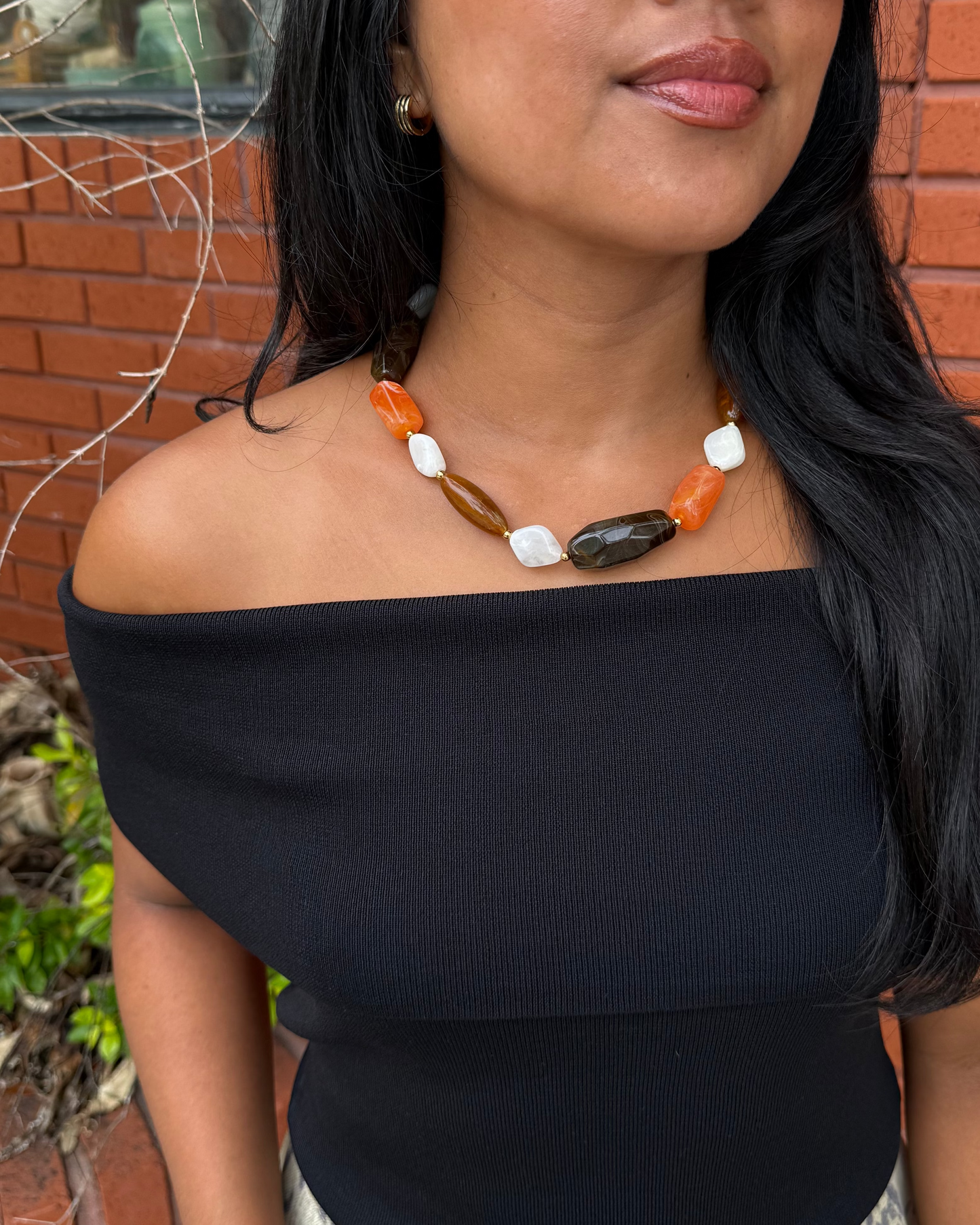Women wearing a beaded orange, brown and white necklace with a black off the shoulder top