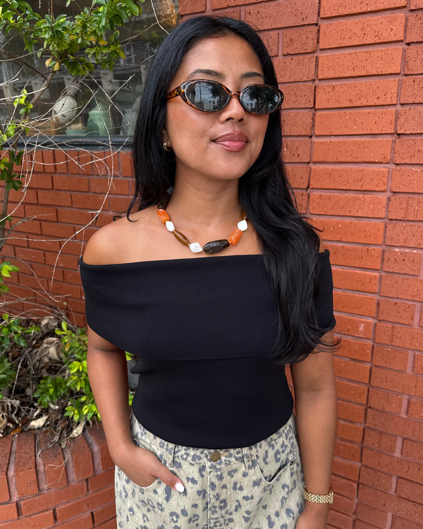 Women wearing a beaded orange, brown and white necklace with a black off the shoulder top and leopard pants