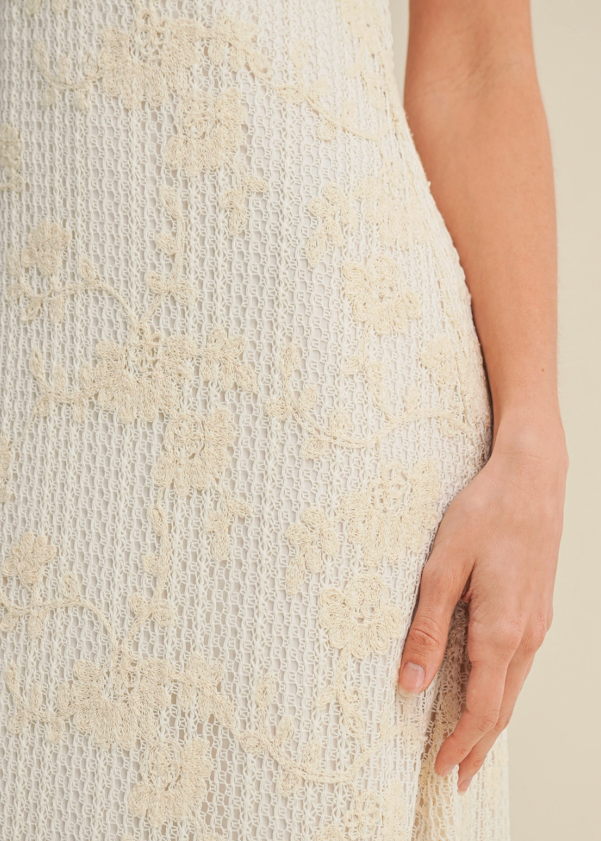 Close-up of a textured beige dress with a hand touching the fabric.