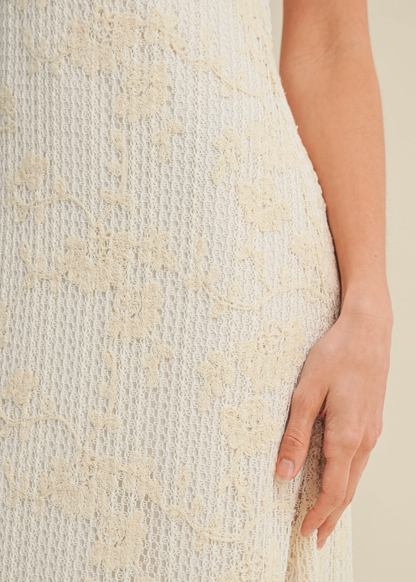 Close-up of a textured beige dress with a hand touching the fabric.