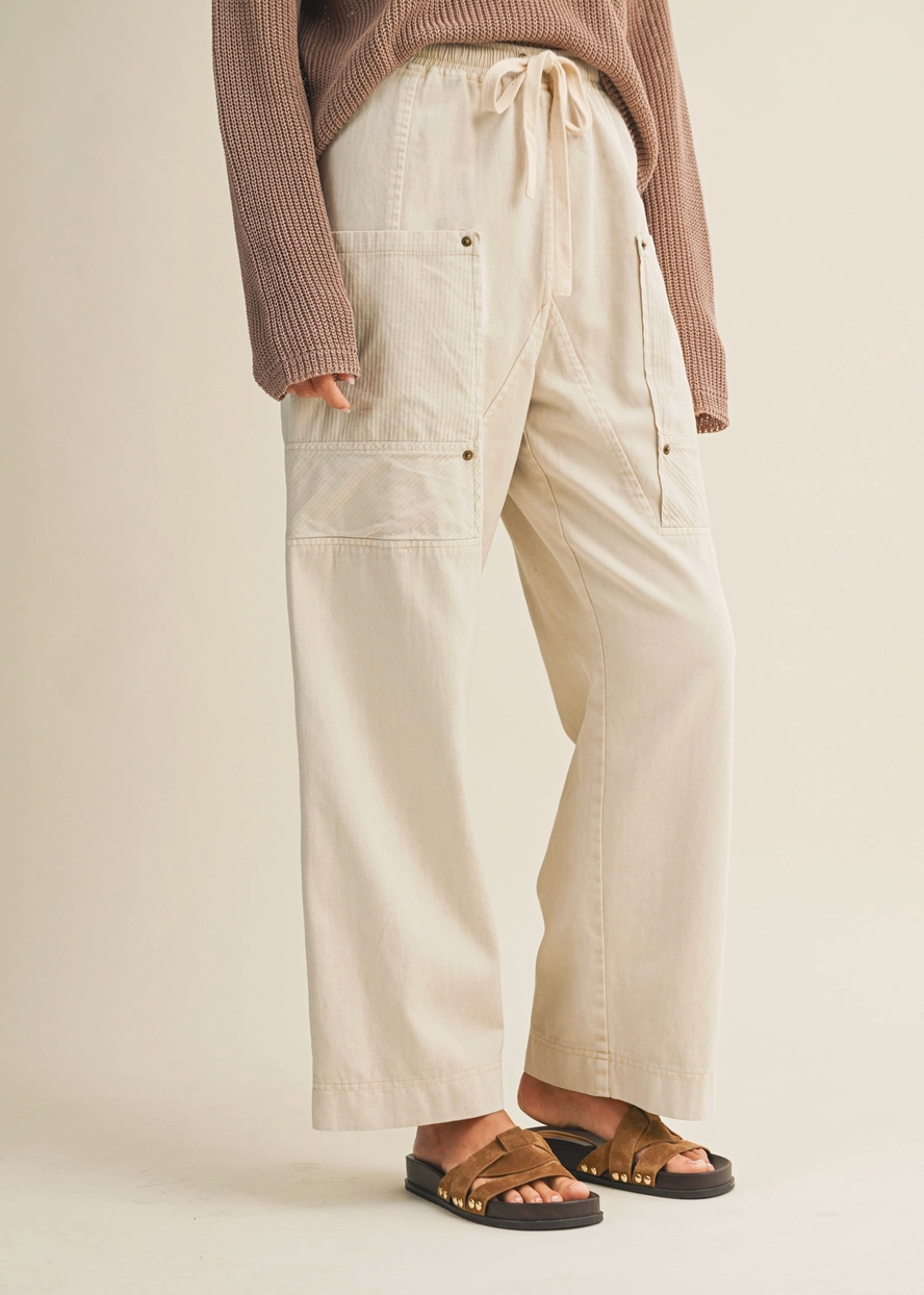 Person wearing beige cargo pants and a brown sweater on a plain background