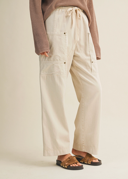 Person wearing beige cargo pants and a brown sweater on a plain background