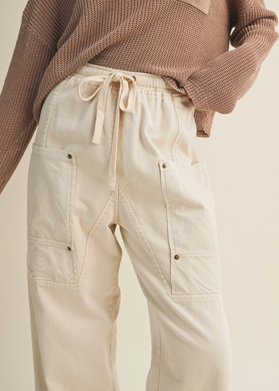 Beige pants with a drawstring waist worn over a brown sweater on a neutral background