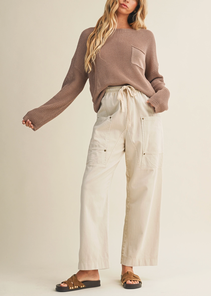 Woman wearing a brown sweater and beige pants on a plain background