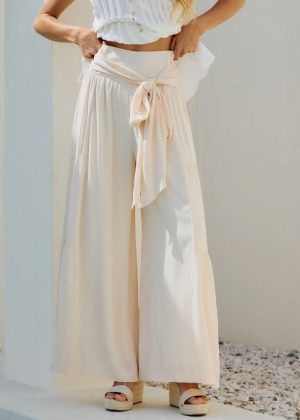 Woman wearing a white sleeveless top and beige wide-leg pants on a minimal background