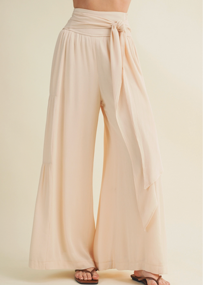 Beige wide-leg pants with a tie waist on a plain background