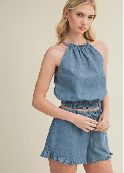 Woman wearing a denim top and shorts against a neutral background