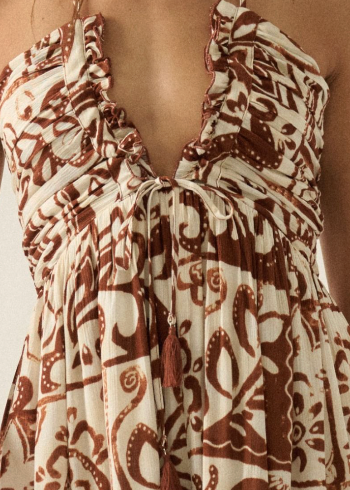 Patterned jumpsuit with a deep neckline and tassels on a neutral background