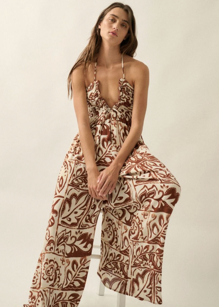 Woman wearing a patterned jumpsuit sitting on a chair against a plain background