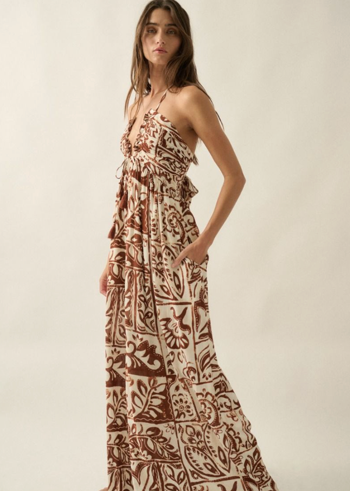 Woman wearing a long, patterned jumpsuit against a plain background