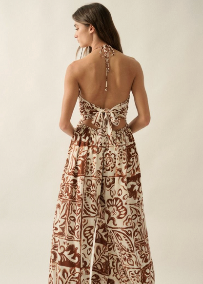 Woman wearing a patterned jumpsuit with a backless design on a plain background