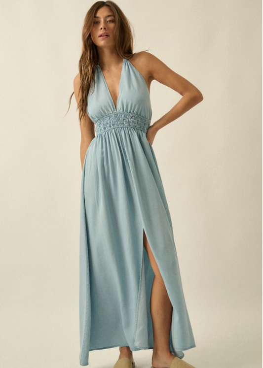 Woman wearing a light blue denim dress with a slit on a beige background