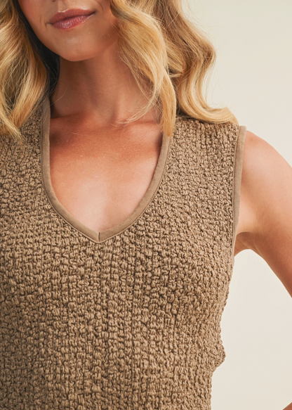 Woman wearing a textured beige sleeveless top against a neutral background