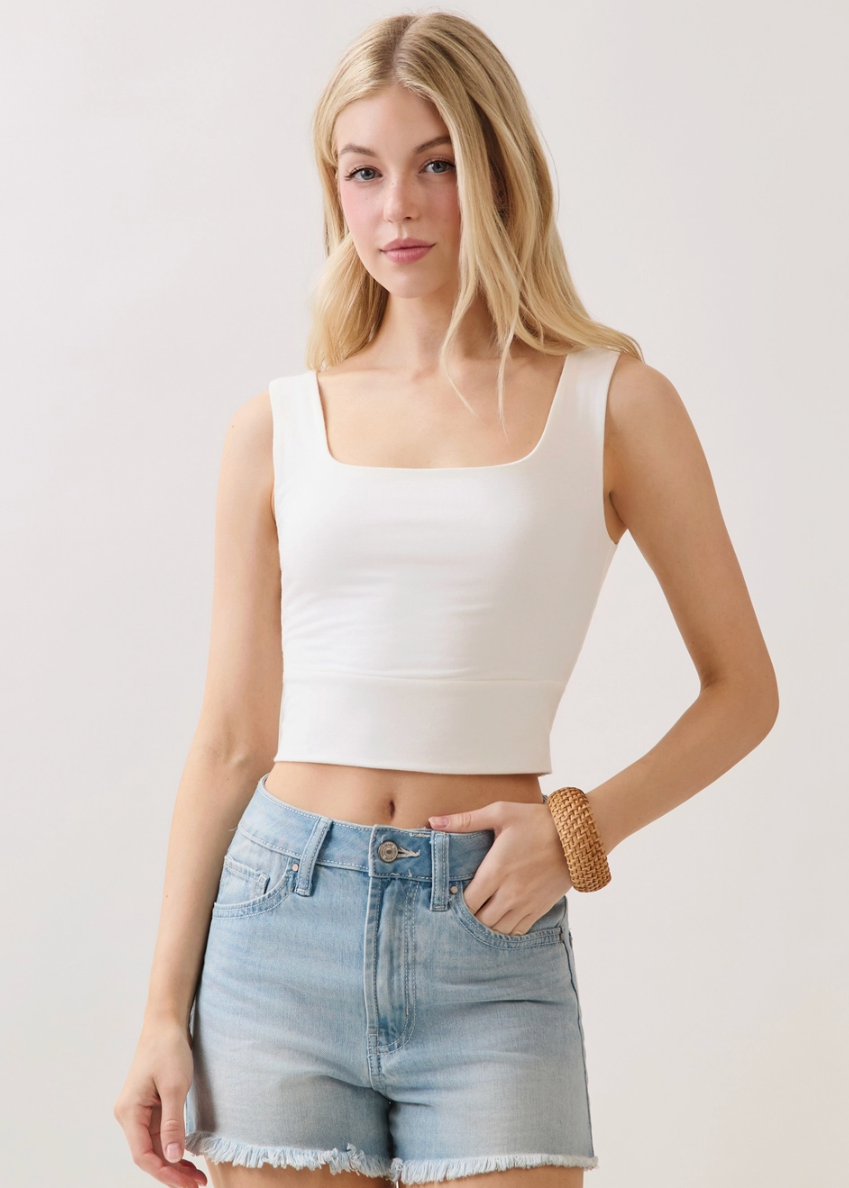 Woman wearing a white tank top and denim shorts on a plain background