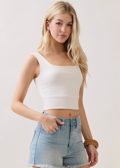 Woman wearing a white tank top and denim shorts against a plain background